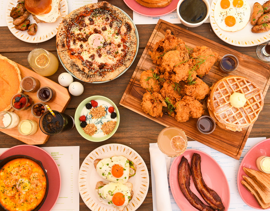 A spread of breakfast waffles, eggs, chicken, and other foods across a table.